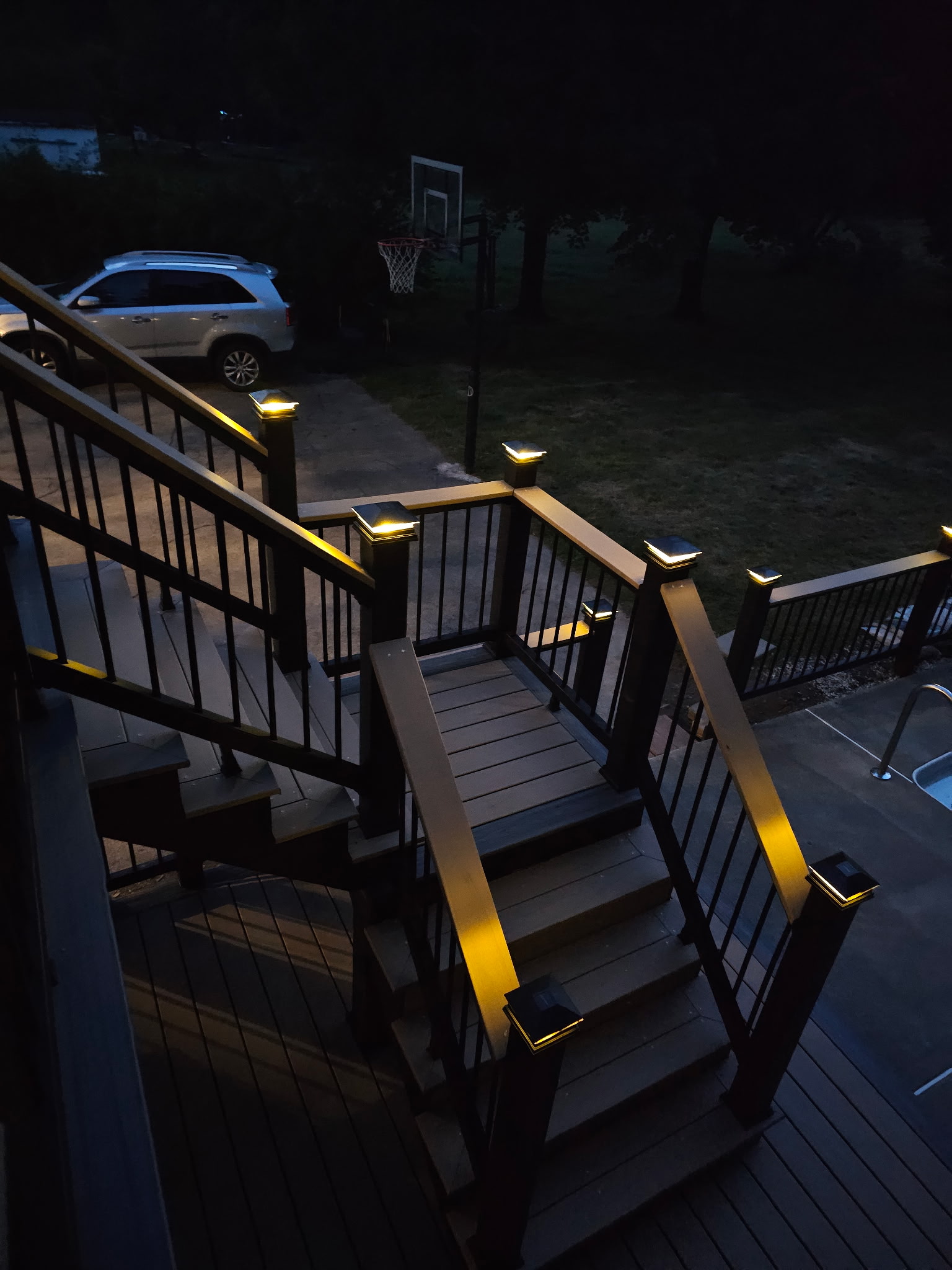 Composite deck stairs with a landing, black aluminum railings and solar post cap lights at night