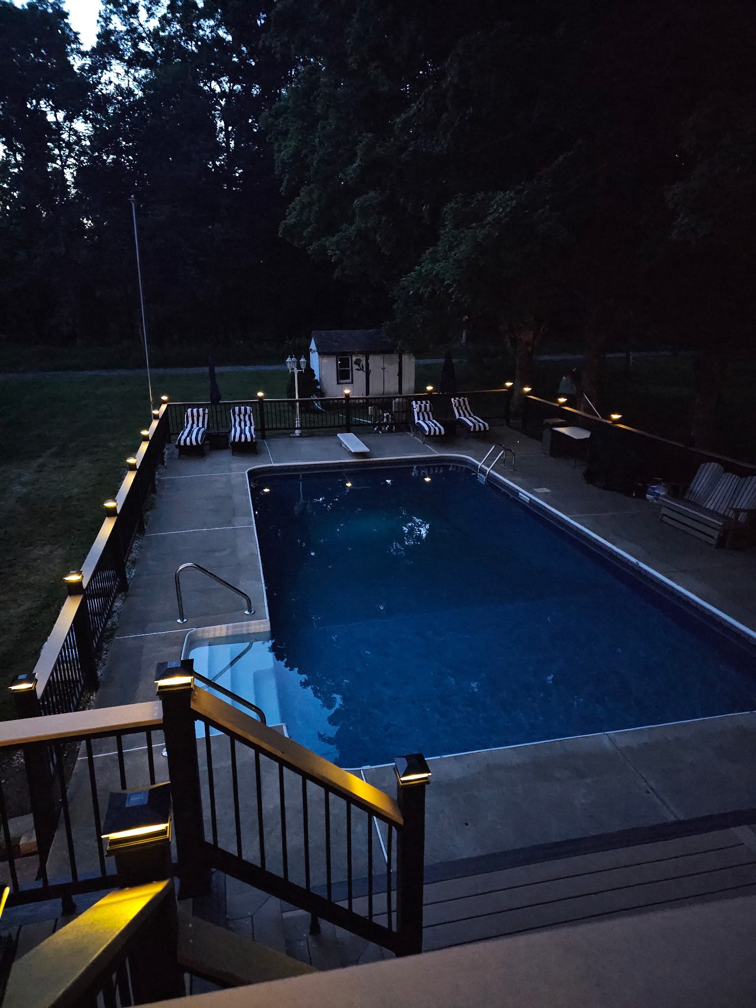 View from a new deck over an in-ground pool with lit railing posts around the pool fence