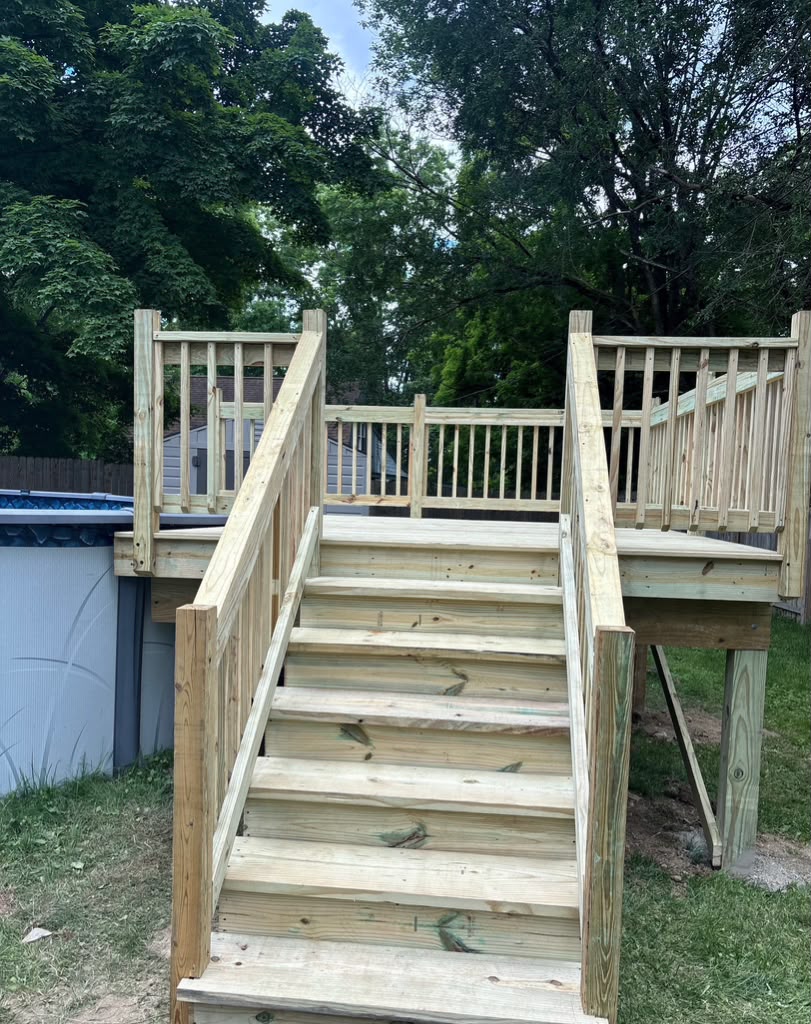 New pressure-treated wood pool deck with wide stairs and wood balusters beside an above-ground pool