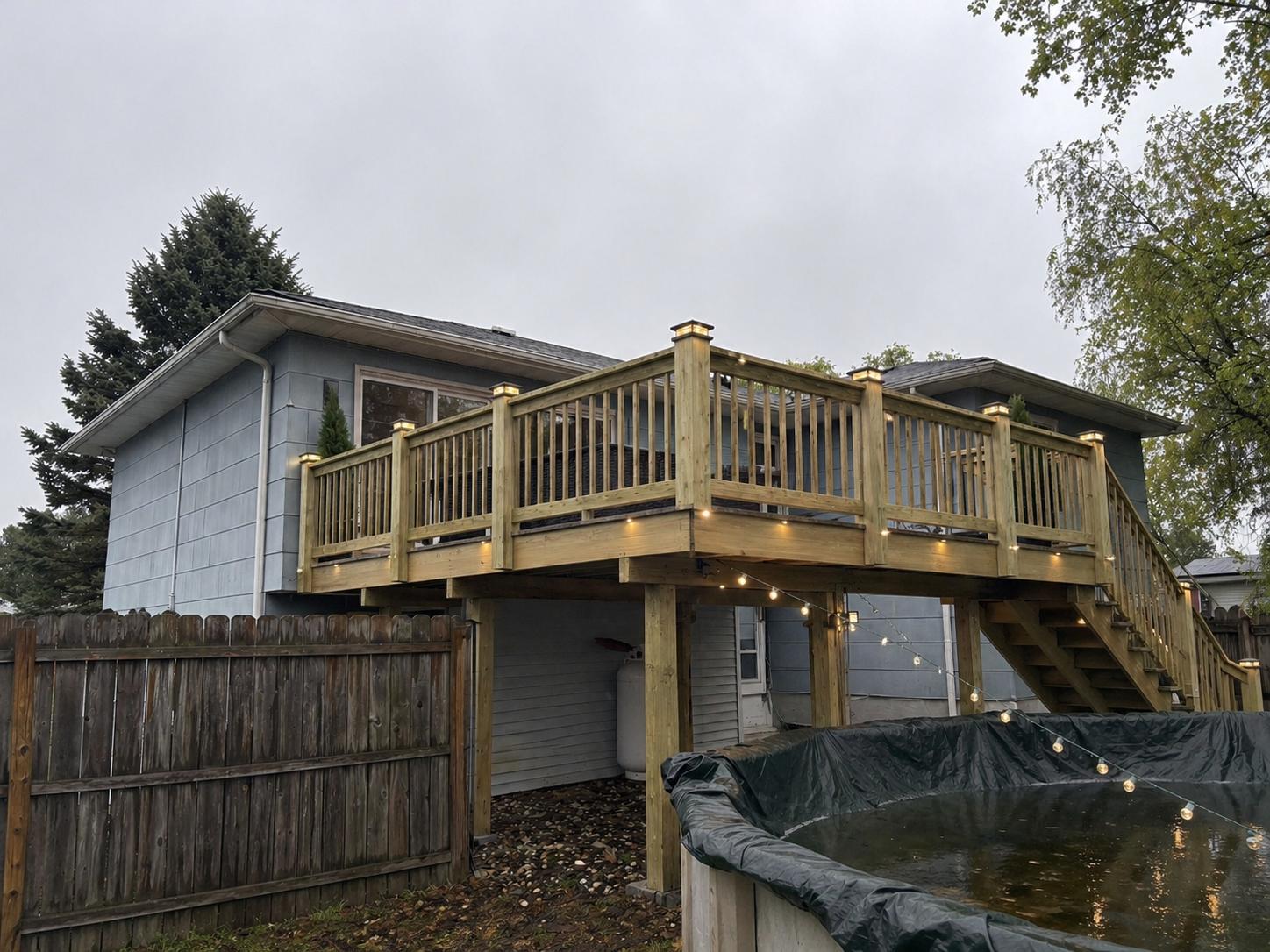 Elevated pressure-treated wood deck with stairs, wood railings and post cap lights over a backyard pool