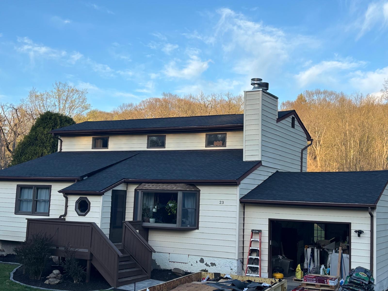 Split-level home with a new charcoal architectural shingle roof and chimney flashing, materials still on site