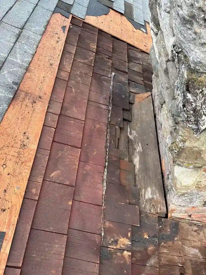 Roofer inspecting deteriorated sheathing around stone chimney base