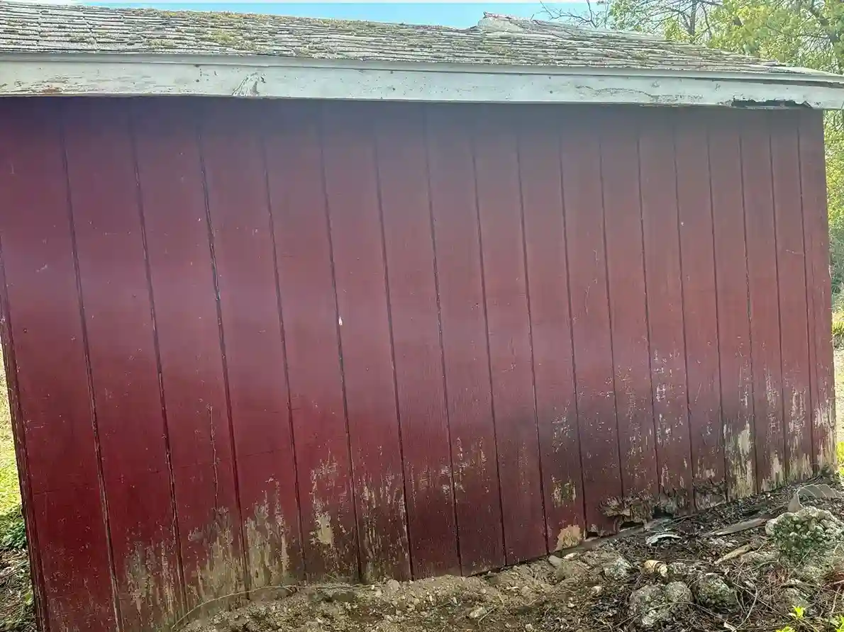 Weathered red barn siding with severe water rot at the base